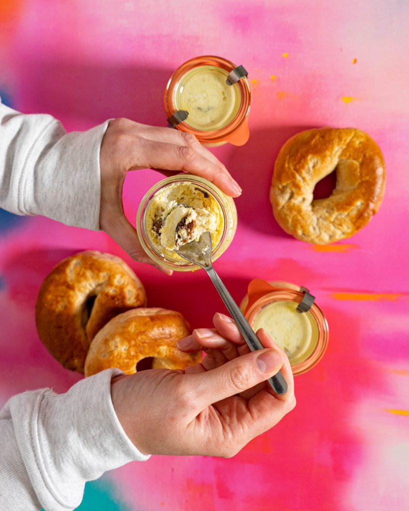 Hands scooping bite of egg bite on pink surface with bagels