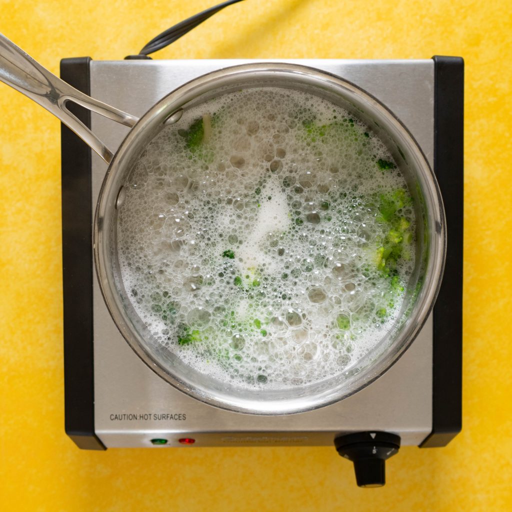 Broccoli and noodles boiling in a pot on yellow surface