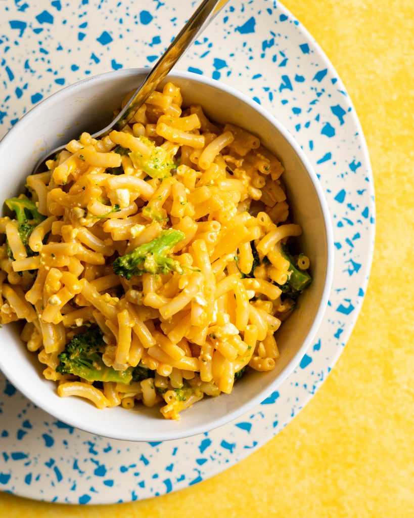 Healthified mac and cheese with broccoli in a white bowl on a blue and white plate on a yellow surface