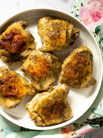 Cooked chicken thighs on white platter on floral napkin