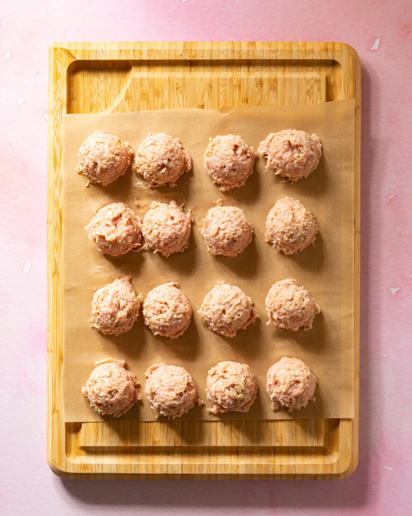 Sous vide meatballs on parchment paper on cutting board on pink surface