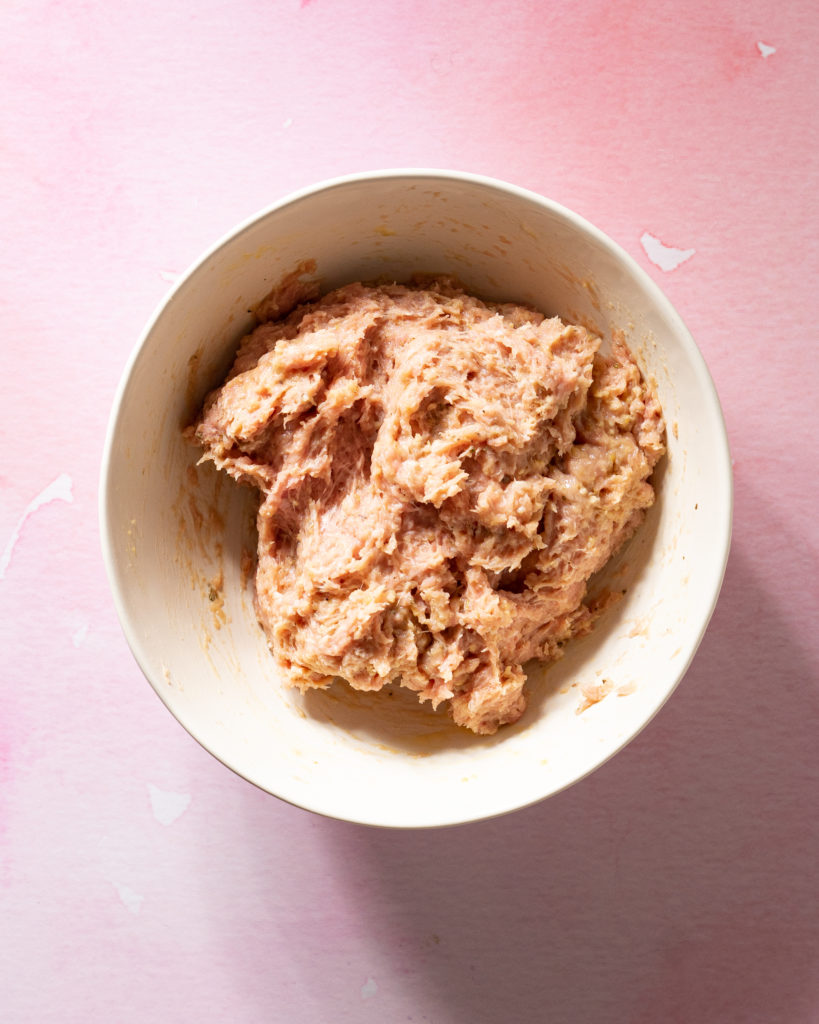 Mixed meatball mixture in white bowl on pink surface