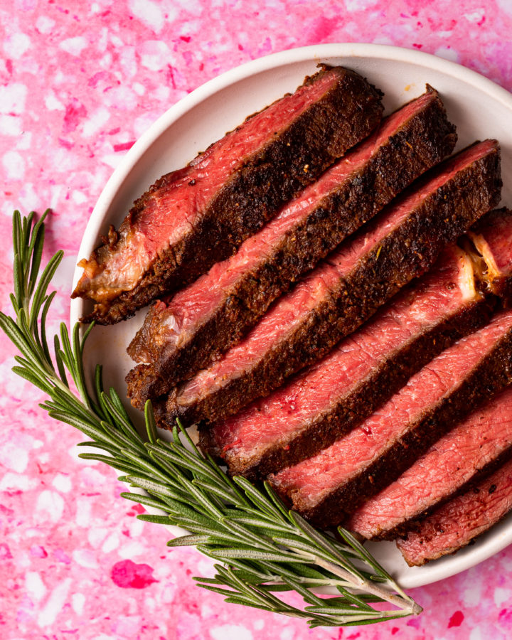 Sliced steak cooked from frozen on a white plate on pink background