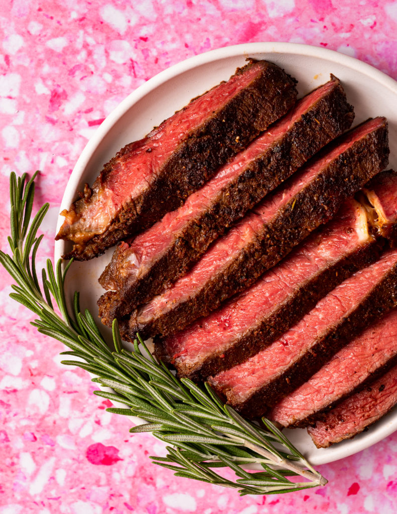 Sliced steak cooked from frozen on a white plate on pink background