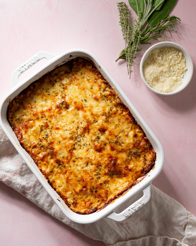 Potatoes au gratin with gruyere and thyme in baking dish on pink surface