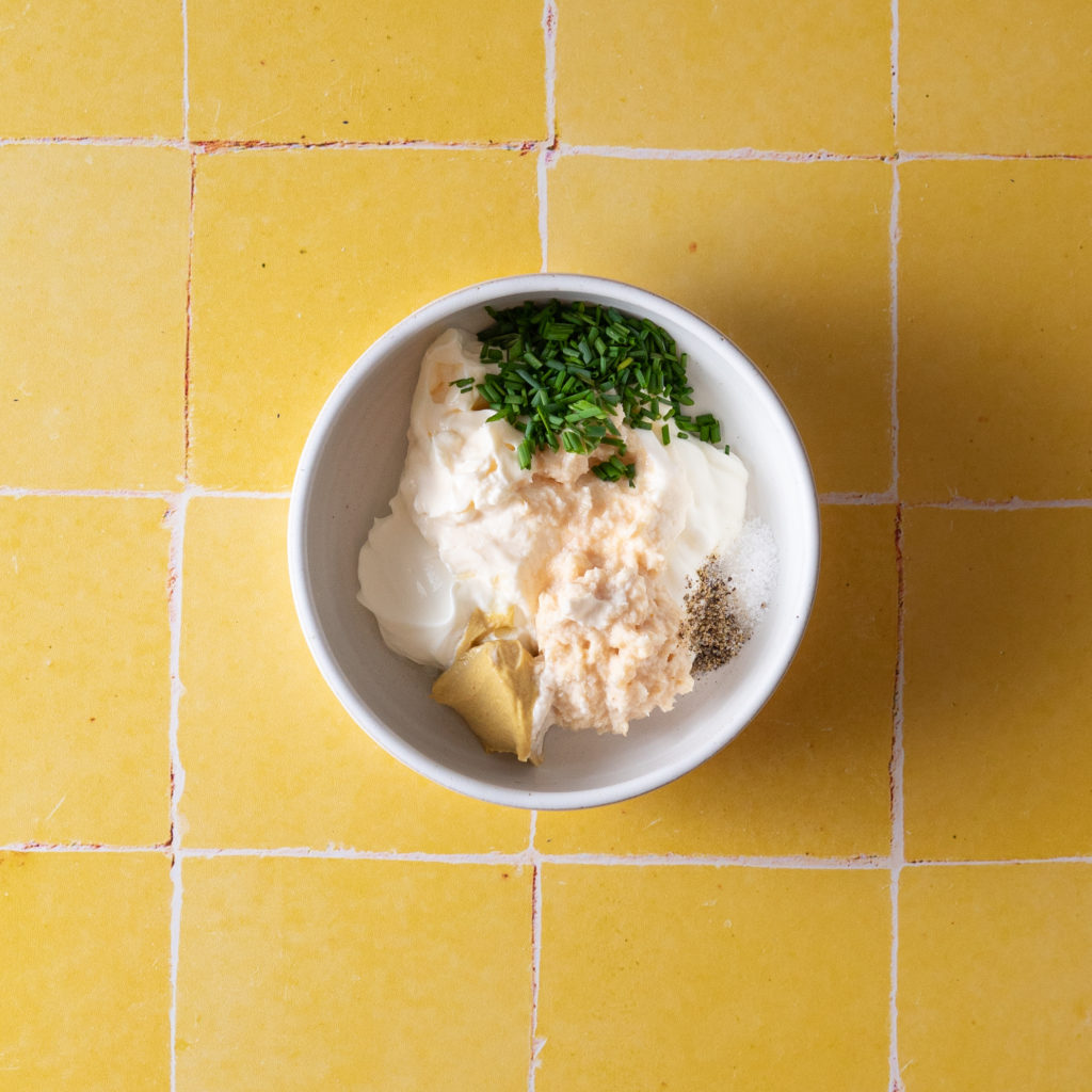 Creamy horseradish sauce ingredients in bowl on yellow tile.