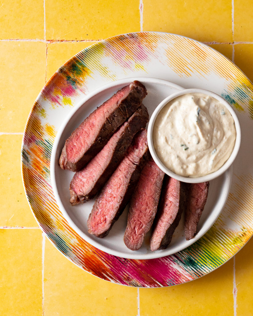 Sliced steak on white plate with bowl of horseradish sauce.