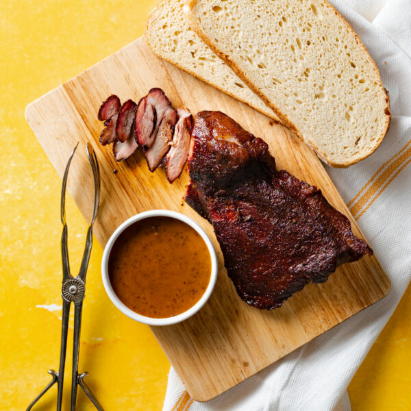 Sous vide and smoked pork brisket on wood cutting board served with bbq sauce and sliced bread.