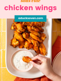 Sous vide chicken wings tossed in buffalo sauce on a white platter with a person dipping a wing into a bowl of ranch dip.