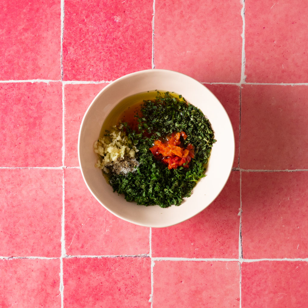 Chimichurri ingredients in pink bowl on pink tile background