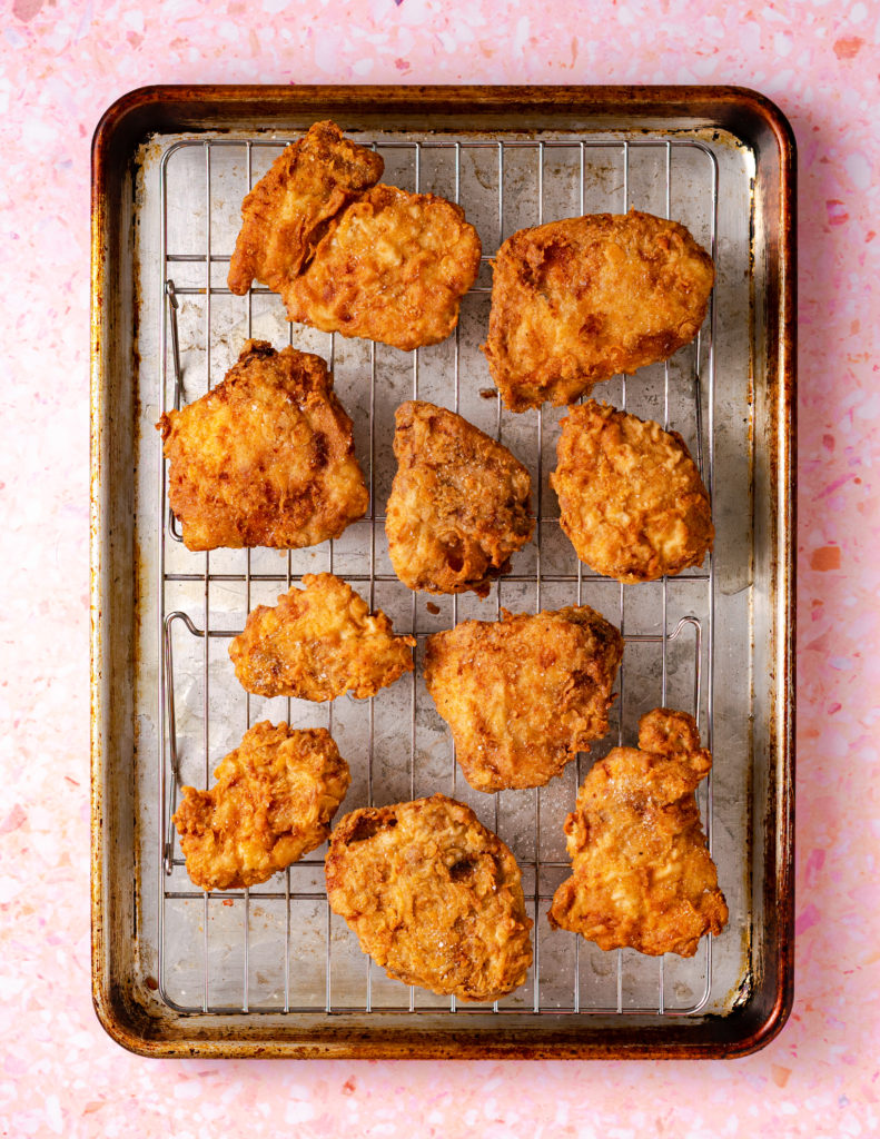 Sous vide fried chicken on wire rack on baking sheet on pink background