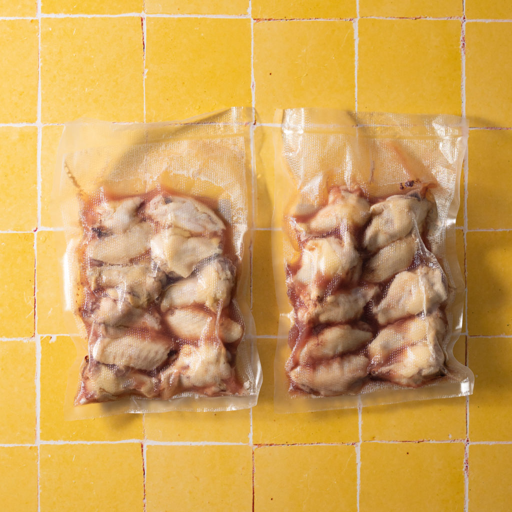 Vacuum sealed cooked chicken wings on yellow tiled surface.