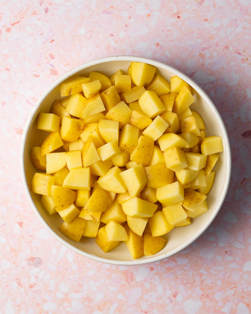 Diced yellow potatoes in bowl on pink surface.