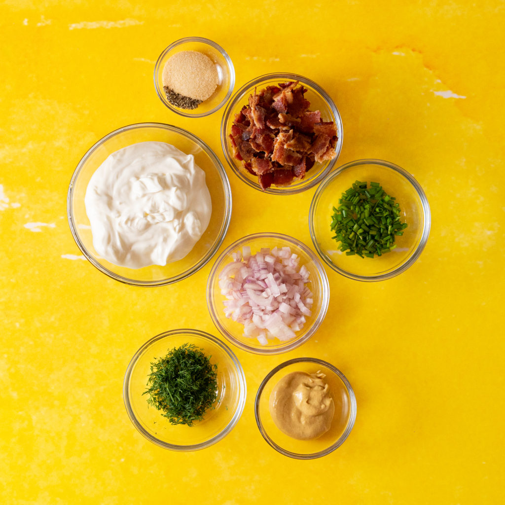 Dressing ingredients for potato salad on yellow surface.