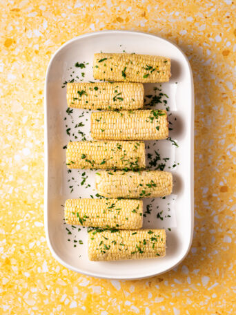 Corn on the cob on white platter on yellow surface.