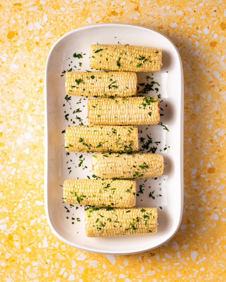 Corn on the cob on white platter on yellow surface.