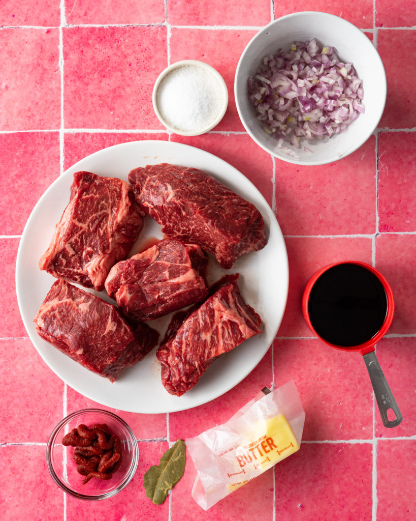 Ingredients for sous vide short ribs on pink surface.