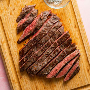 Sliced sous vide flank steak on a wood cutting board with a bowl of herby salt.