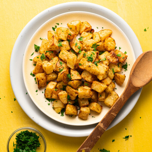 Sous vide potatoes on a plate garnished with parsley on yellow surface with wooden serving spoon