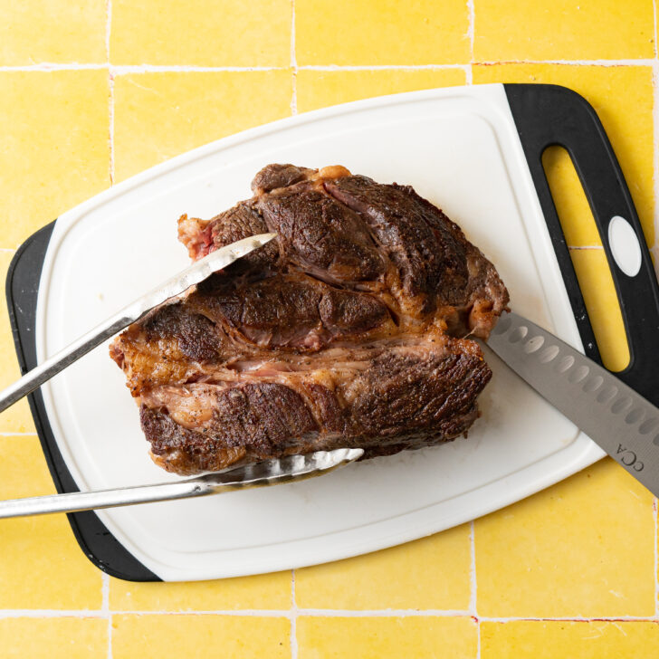 Seared chuck roast on cutting board with knife and tongs