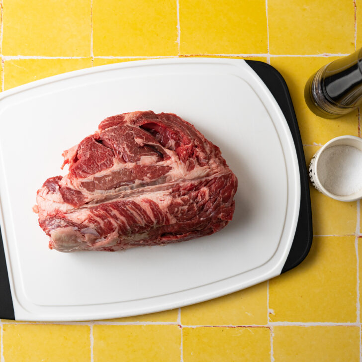 Chuck roast on cutting board with salt and pepper.