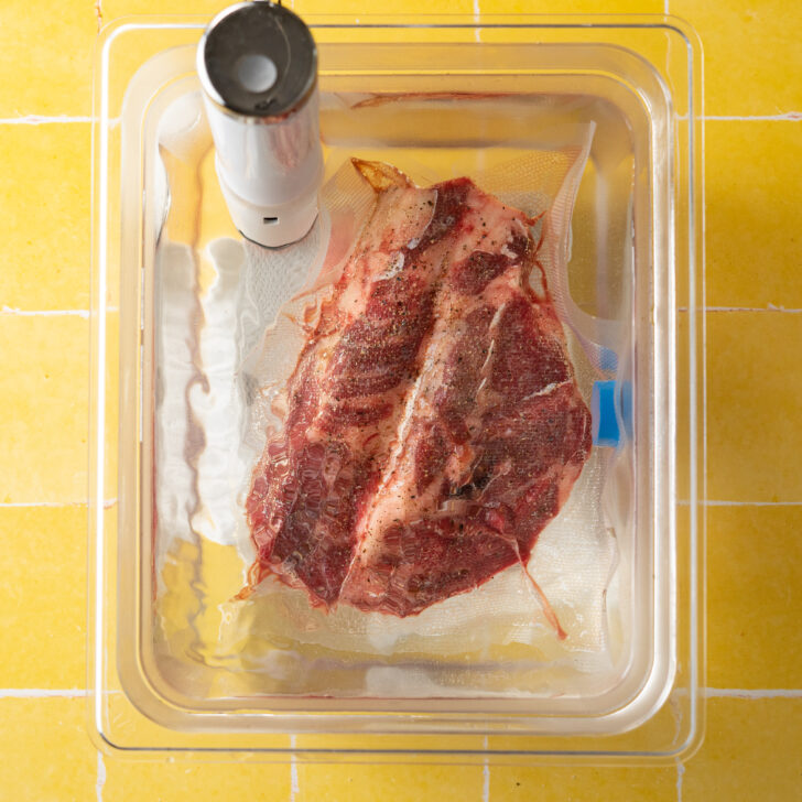 Vacuum sealed chuck roast in sous vide water bath on yellow surface