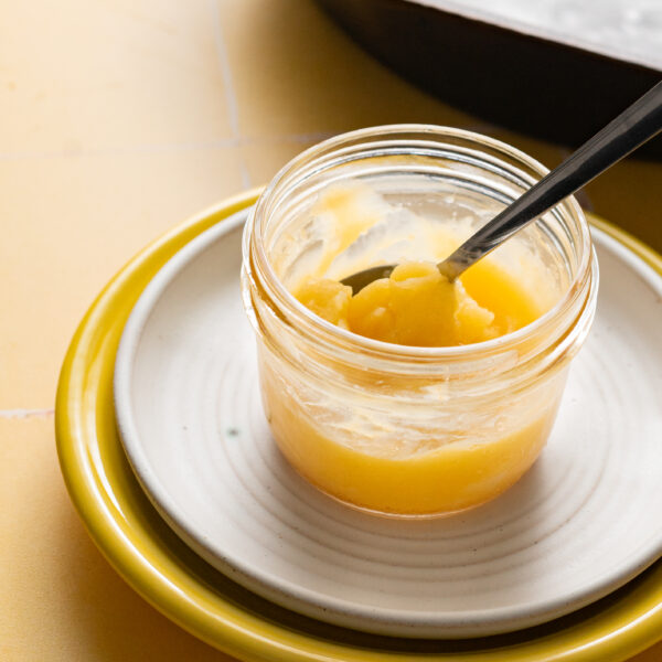 Homemade ghee in glass jar on stacked plates.