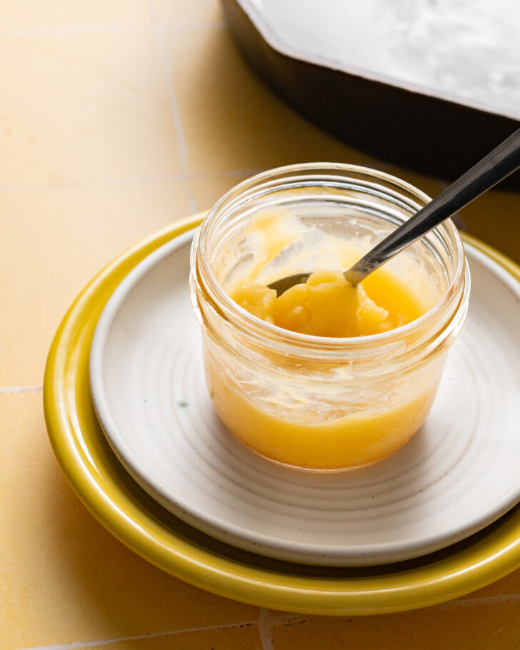 Homemade ghee in jar on stacked plates.