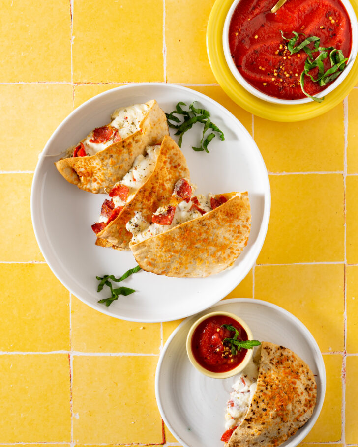Pita calzones on white plate with dipping sauce on a yellow surface.