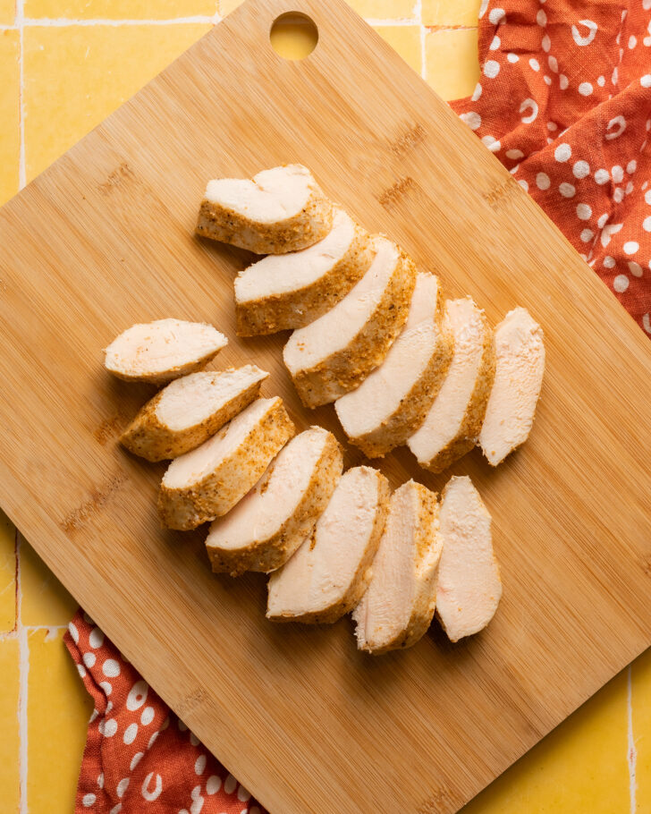 Sous vide chicken breasts sliced on a wood cutting board on yellow surface
