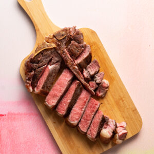 T-bone steak cooked medium rare and sliced on wood cutting board.