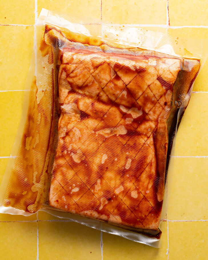 Vacuum sealed pork belly in marinade on yellow tiled surface.