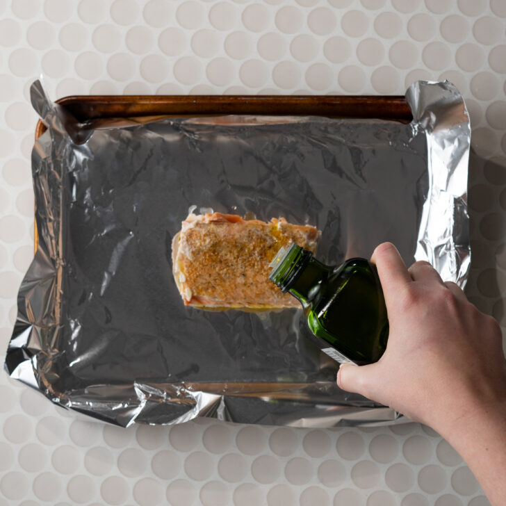 Drizzling olive oil over sous vided salmon on foil lined baking sheet.