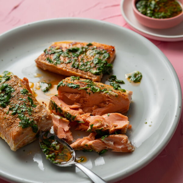 Flaked sous vide salmon on a white plate with chimichurri sauce.