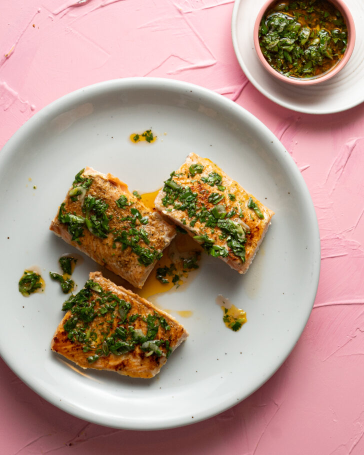 Sous vide salmon on a white plate with chimichurri sauce.