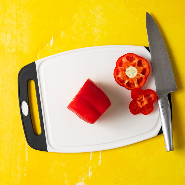 Red bell pepper with top and bottom removed on white cutting board.