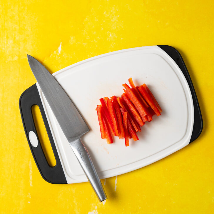 Pile of sliced red bell pepper on white cutting board.