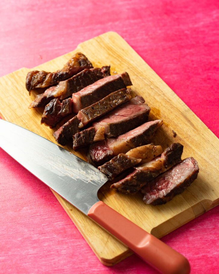 Sliced sous vide ribeye steak on wood cutting board.