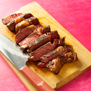 Sliced sous vide ribeye steak on wood cutting board.