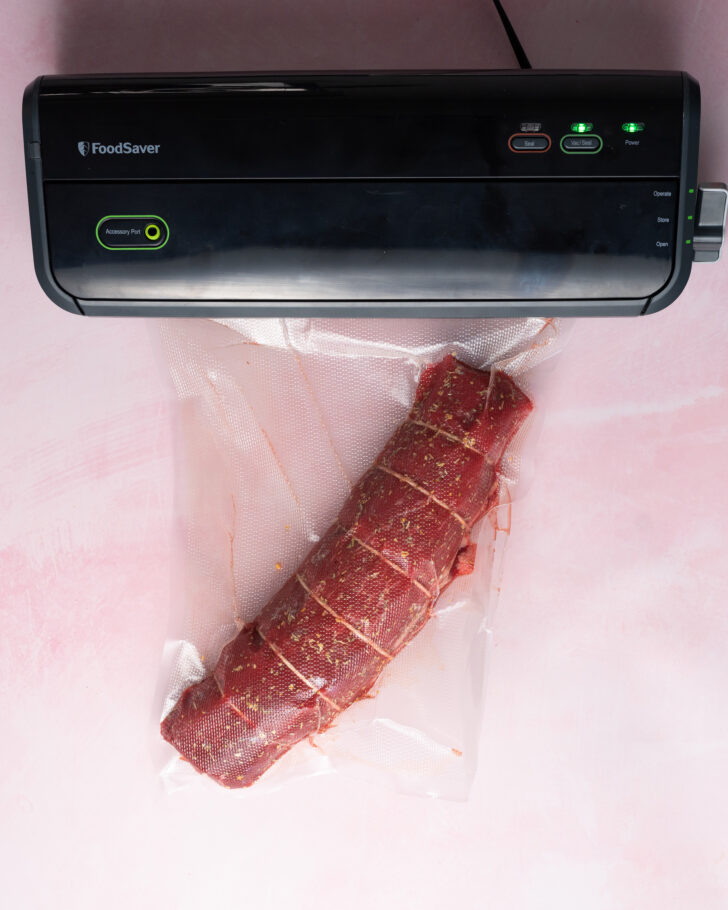Vacuum sealed beef tenderloin on pink surface.
