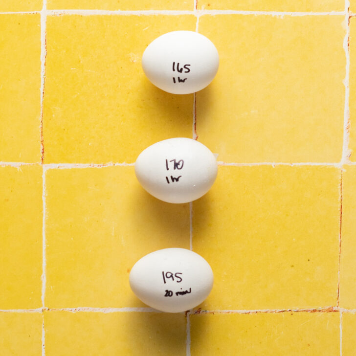 3 eggs with times and temperatures written on them in Sharpie on a yellow tiled surface.