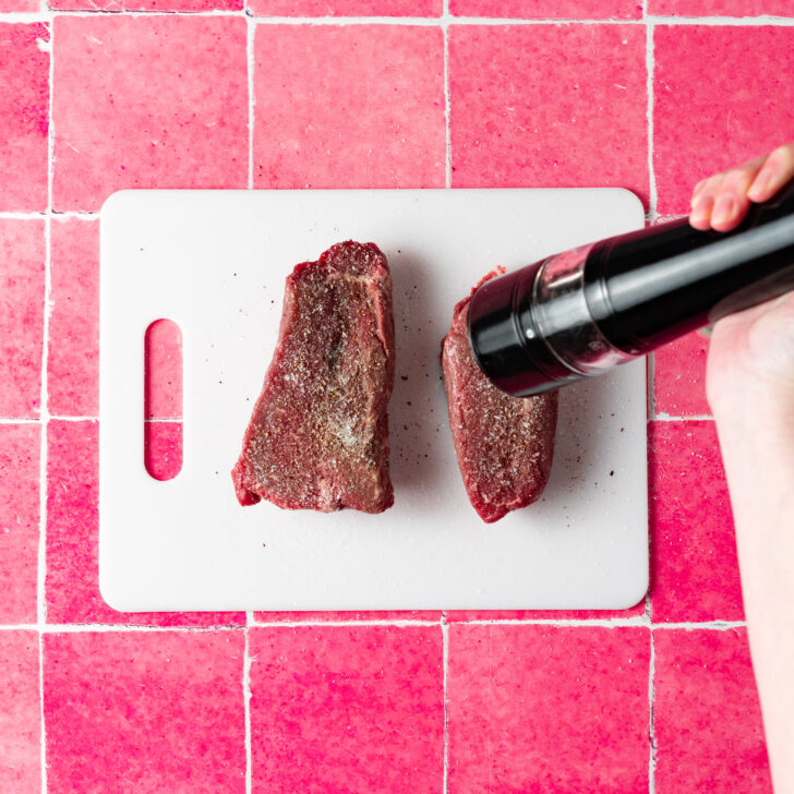 Seasoning sirloin steak with freshly cracked black pepper on cutting board