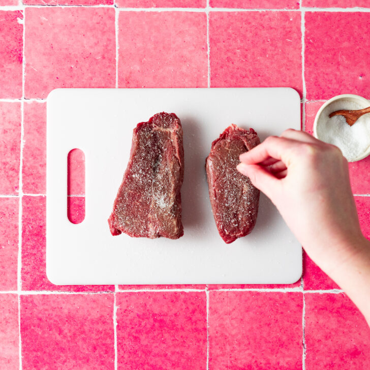 Seasoning sirloin steak with kosher salt on cutting board