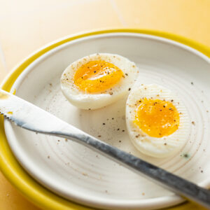 Sous vide soft boiled egg with salt and pepper on white plate.