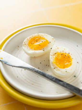 Sous vide soft boiled egg with salt and pepper on white plate.
