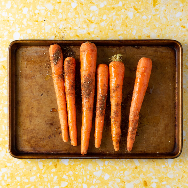 Carrots on rimmed baking sheet with ingredients sprinkled on them.