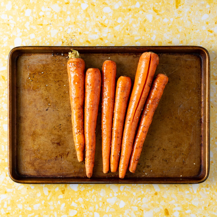 Carrots on rimmed baking sheet tossed in seasoning ingredients.