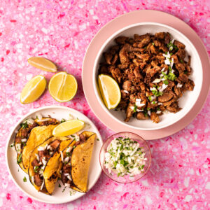 Sous vide carnitas and carnitas tacos on pink surface.