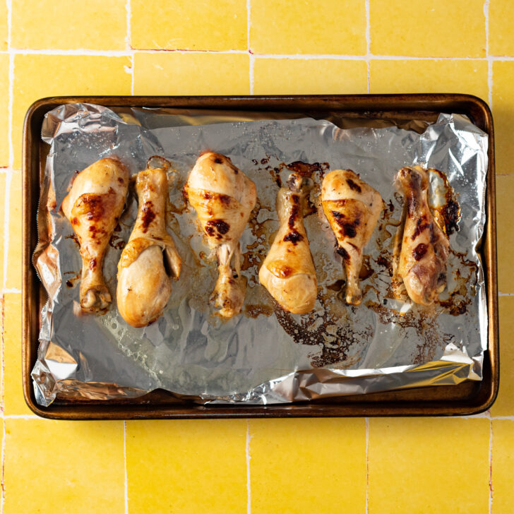 Broiled chicken drumsticks on a foil lined baking sheet.