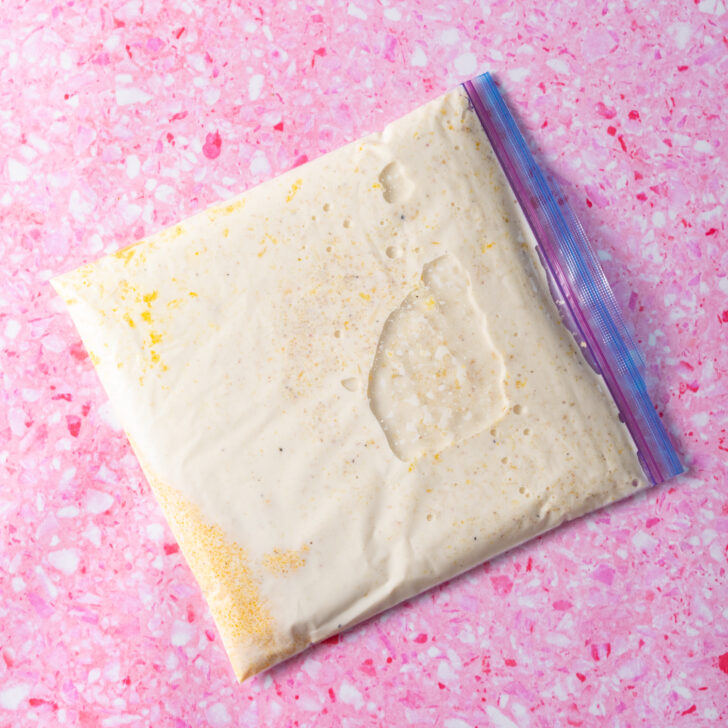 Sealed bag of polenta ingredients with air removed lying down on pink surface.